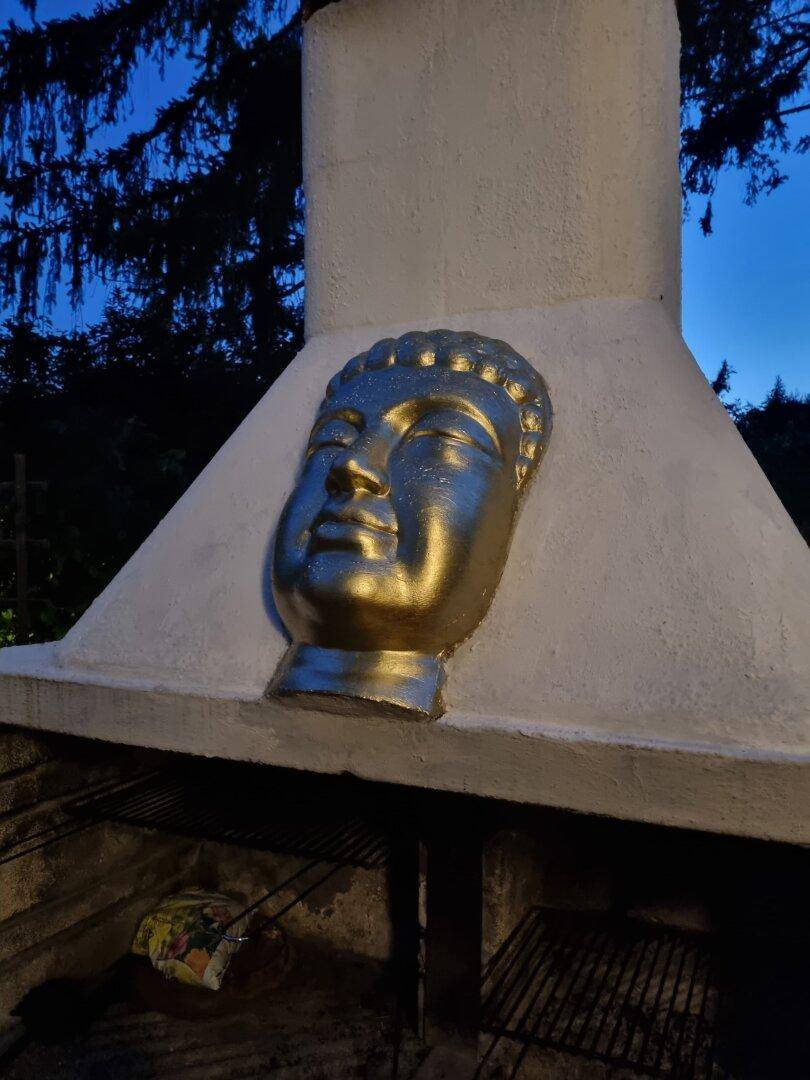Außenkamin mit dekorativer Buddha-Statue in einem Gartenbereich bei Nacht.