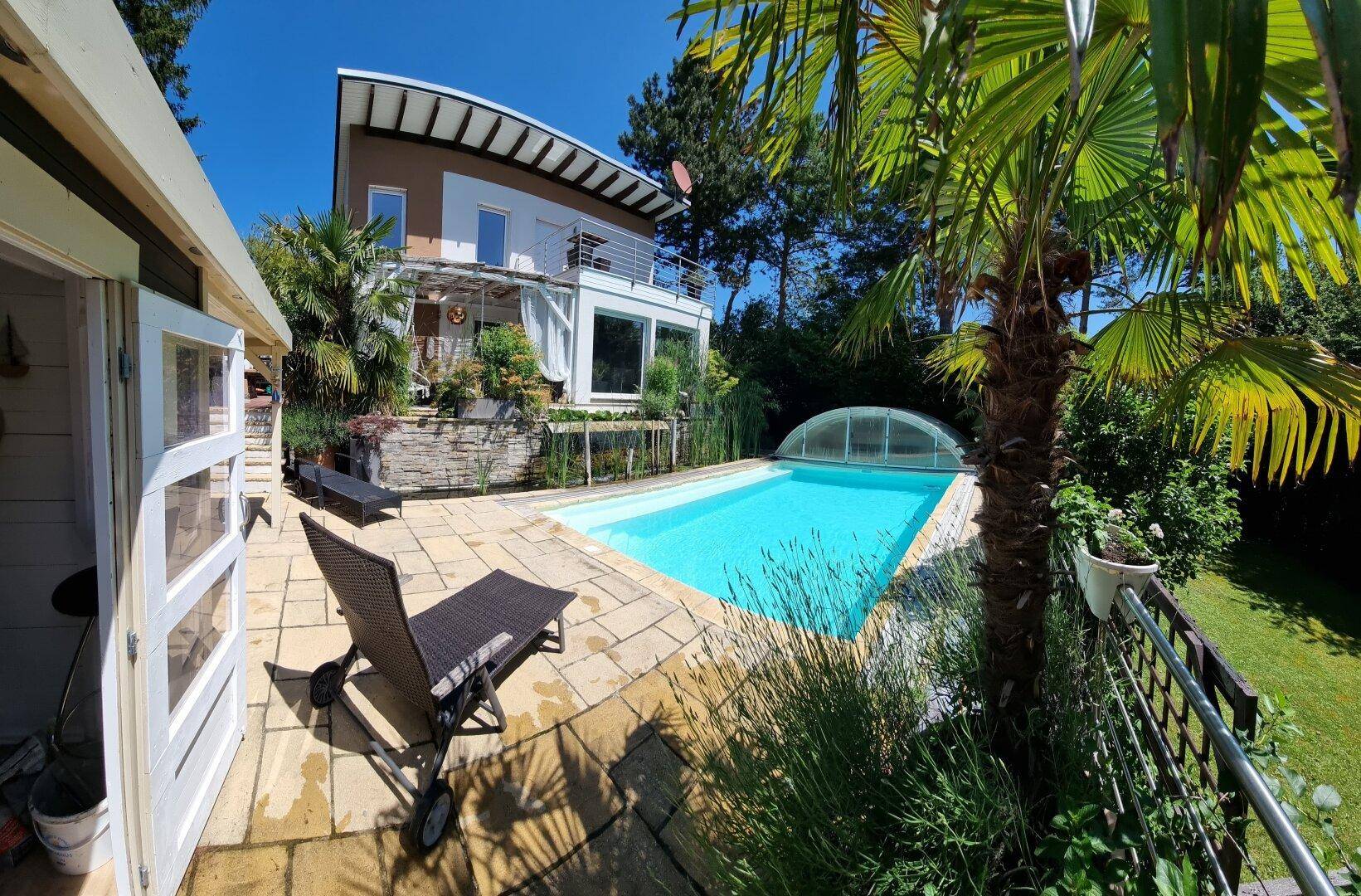 Weitläufiger Gartenbereich mit großem Pool, Liegestühlen und tropischen Pflanzen vor dem Haus.