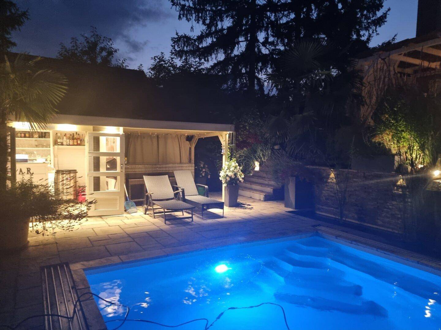 Beleuchteter Poolbereich mit Poolhaus und Liegestühlen bei Nacht, ideal zum Entspannen.