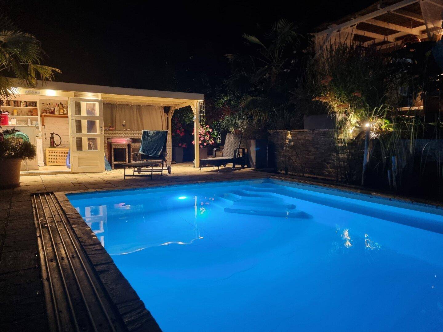 Beleuchteter Poolbereich mit Poolhaus und Liegestühlen bei Nacht, ideal zum Entspannen.