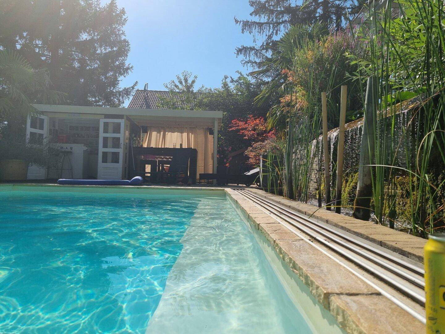 Blauer Pool mit klarem Wasser und einem dekorativen Wasserfall im sonnigen Garten.