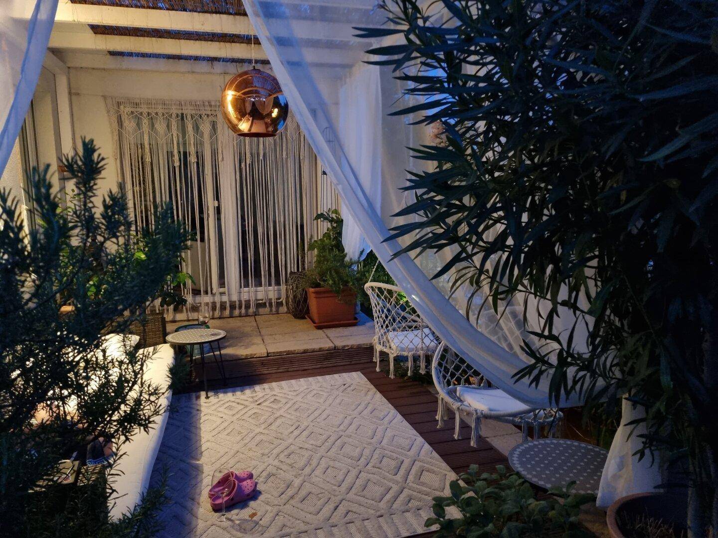 Gemütliche überdachte Terrasse bei Nacht mit Teppich, Hängesesseln und stimmungsvoller Beleuchtung.