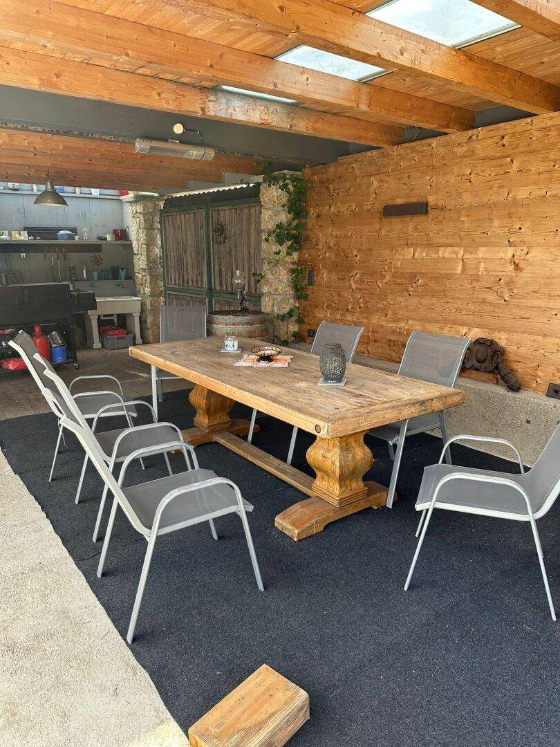Überdachter Essbereich im Freien mit großem Holztisch und Holzdecke, ideal für Mahlzeiten im Grünen.
