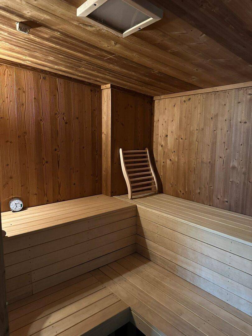 Traditionelle Holzsauna mit mehreren Sitzebenen und einem Thermometer für entspannende Momente.