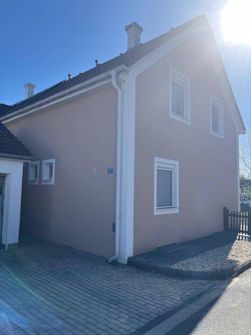 Seitenansicht eines Einfamilienhauses mit gepflasterter Einfahrt und sauberer Fassade bei Sonnenschein.