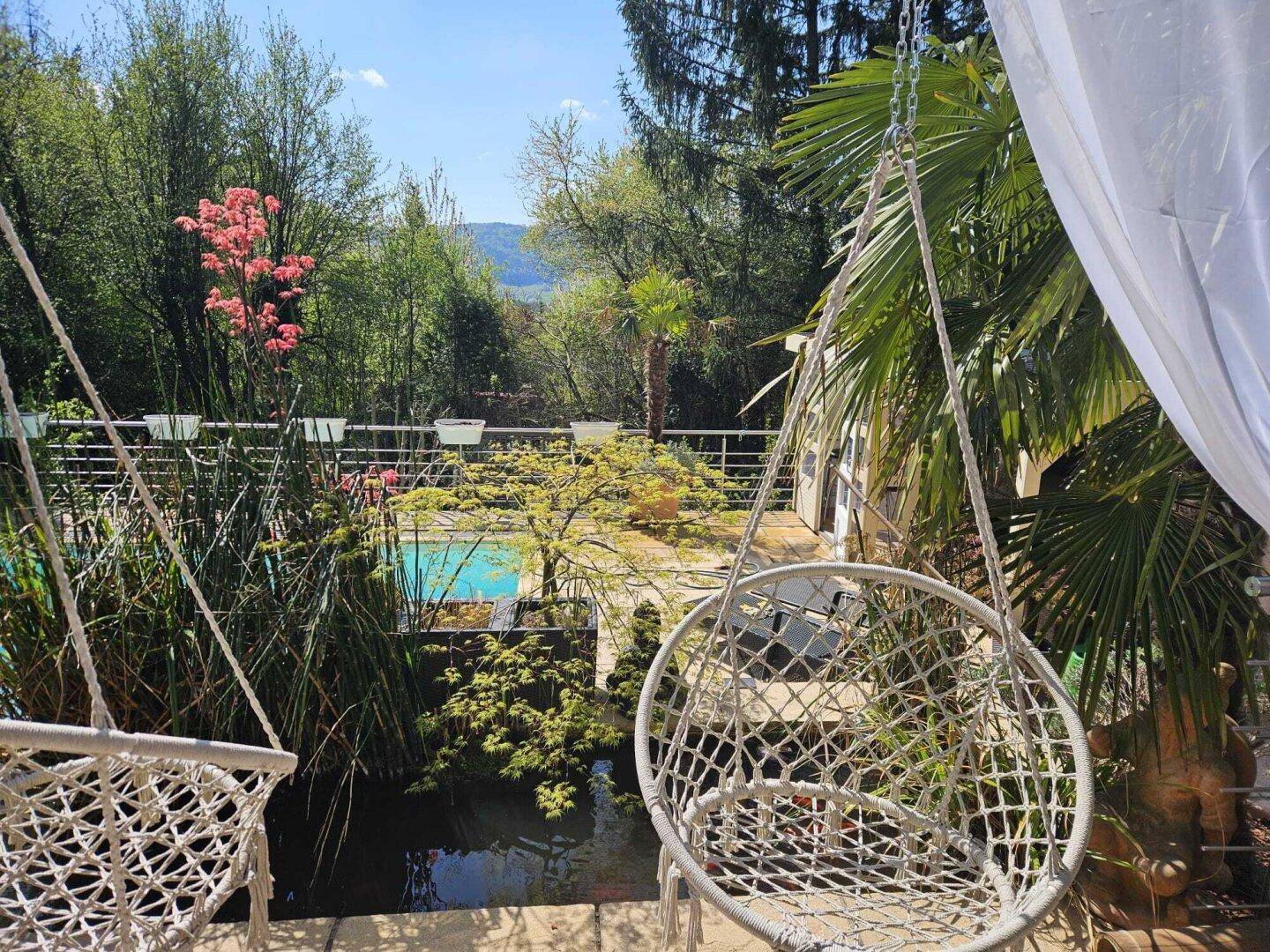 Hängesessel im Garten mit Blick auf den Pool, Teich und die grüne Landschaft.