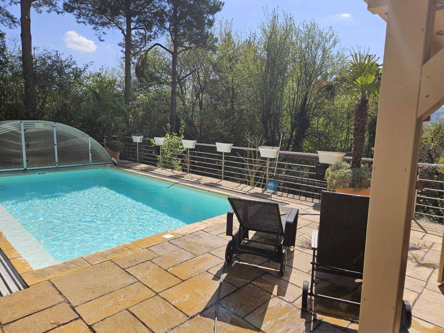 Sonniger Poolbereich mit Liegestühlen und gepflasterter Terrasse, umgeben von Bäumen.