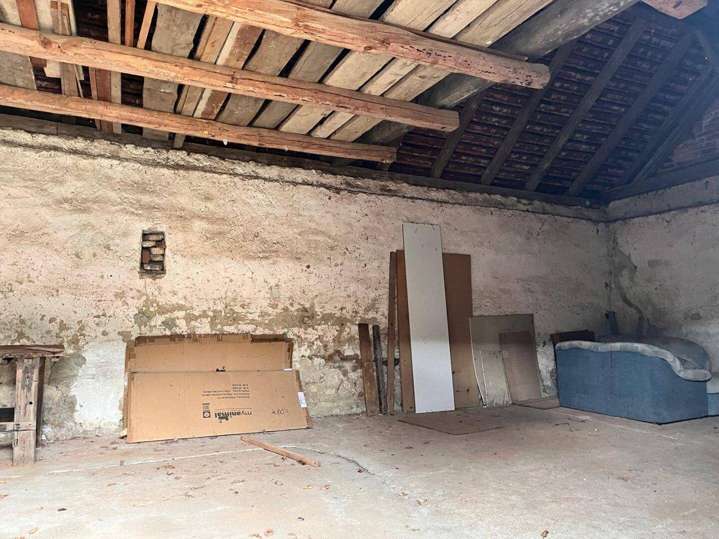 Unausgebauter Dachboden oder Lagerraum mit sichtbaren Holzbalken und rauen Wänden.