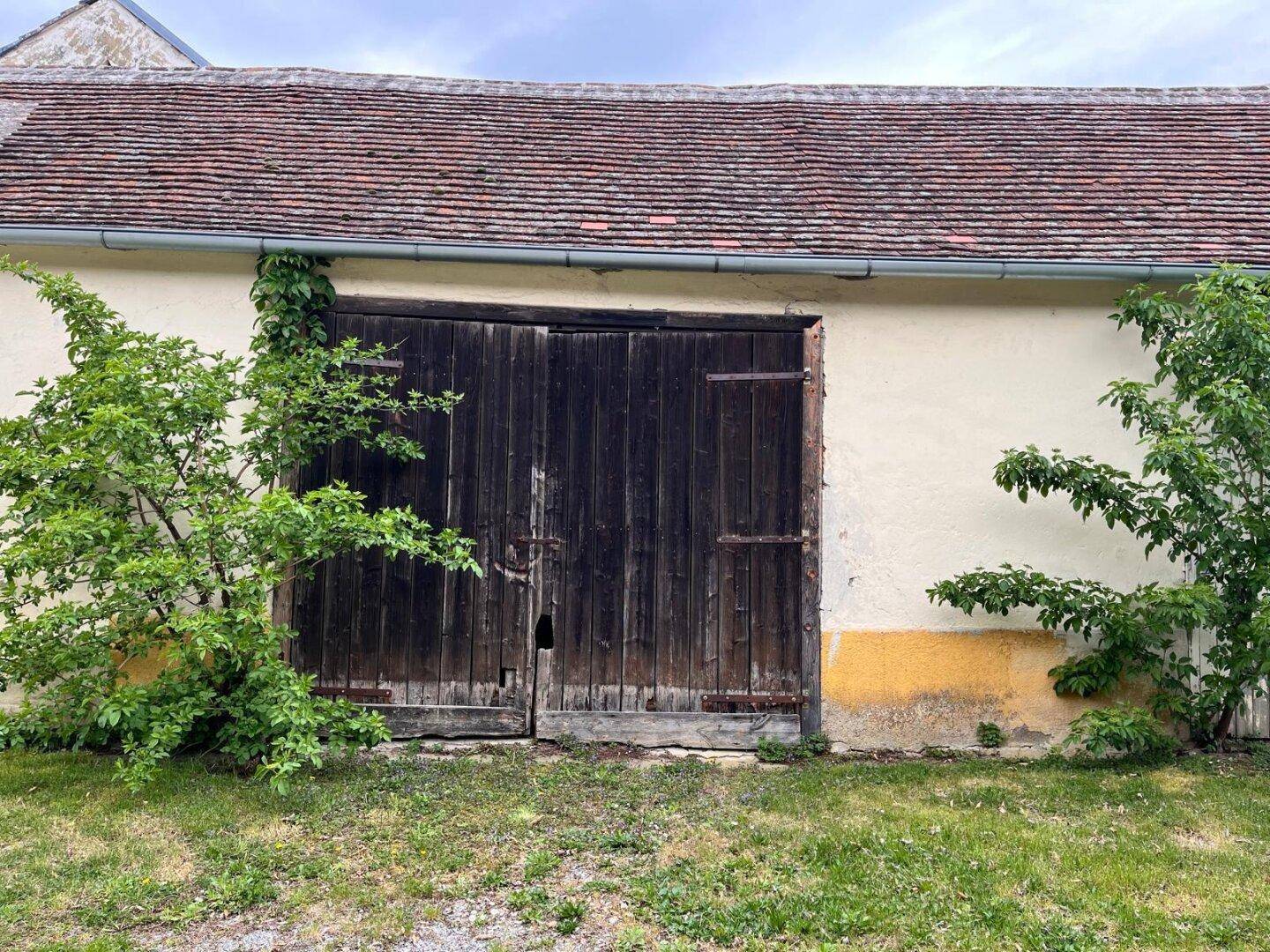 Fassade einer Scheune oder eines großen Nebengebäudes mit rustikalen Holztoren und Ziegeldach.