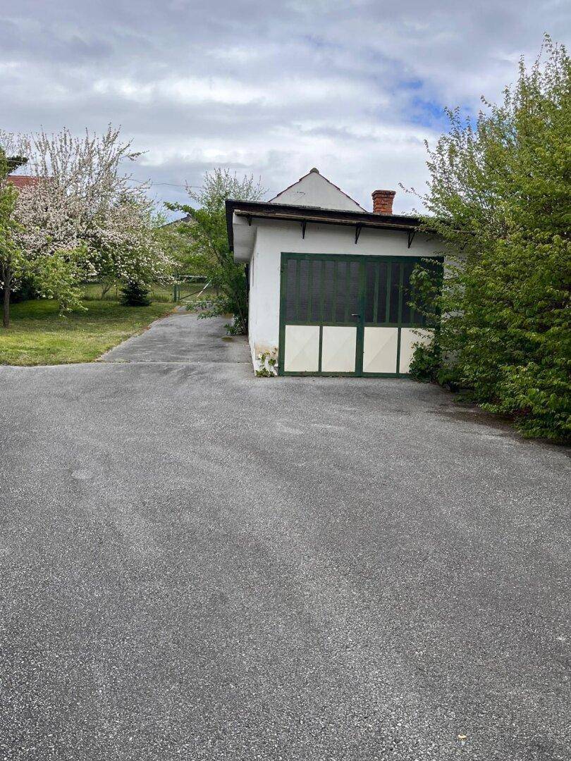 Zufahrt zu einem freistehenden Garagengebäude mit grünen Toren, umgeben von Bäumen.