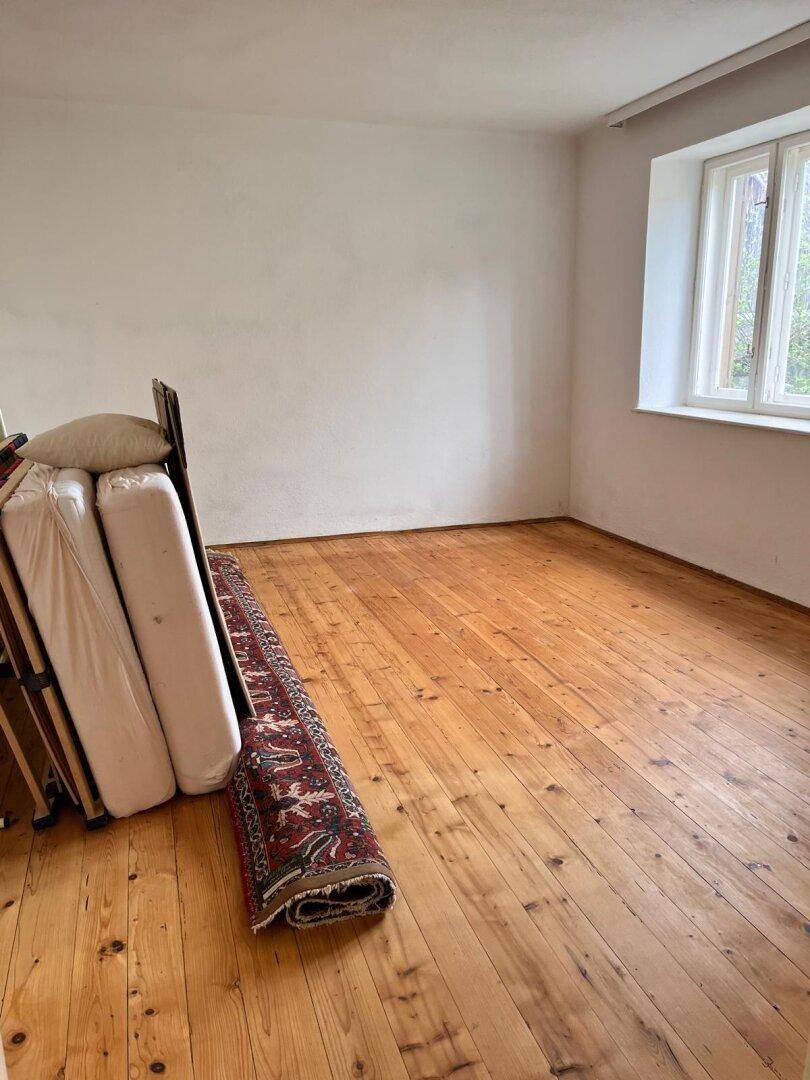 Geräumiges Zimmer mit Holzdielenboden und Fenster, bereit zur individuellen Gestaltung.