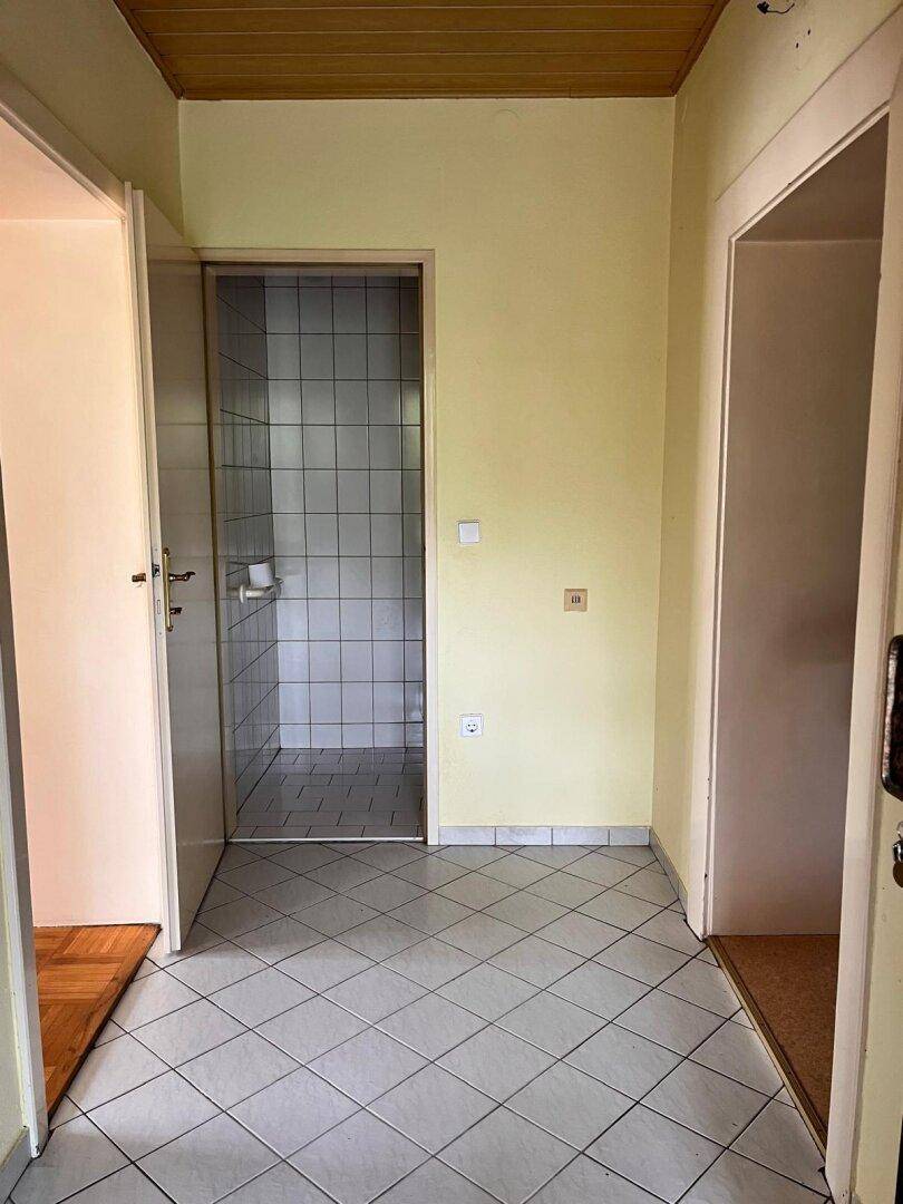 Flur mit Fliesenboden, der zu einem Badezimmer mit weißen Wand- und Bodenfliesen führt.