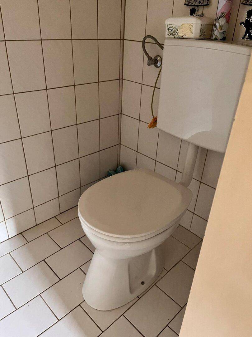 Einfaches WC mit weißen Fliesen an Wänden und Boden, funktional und sauber.