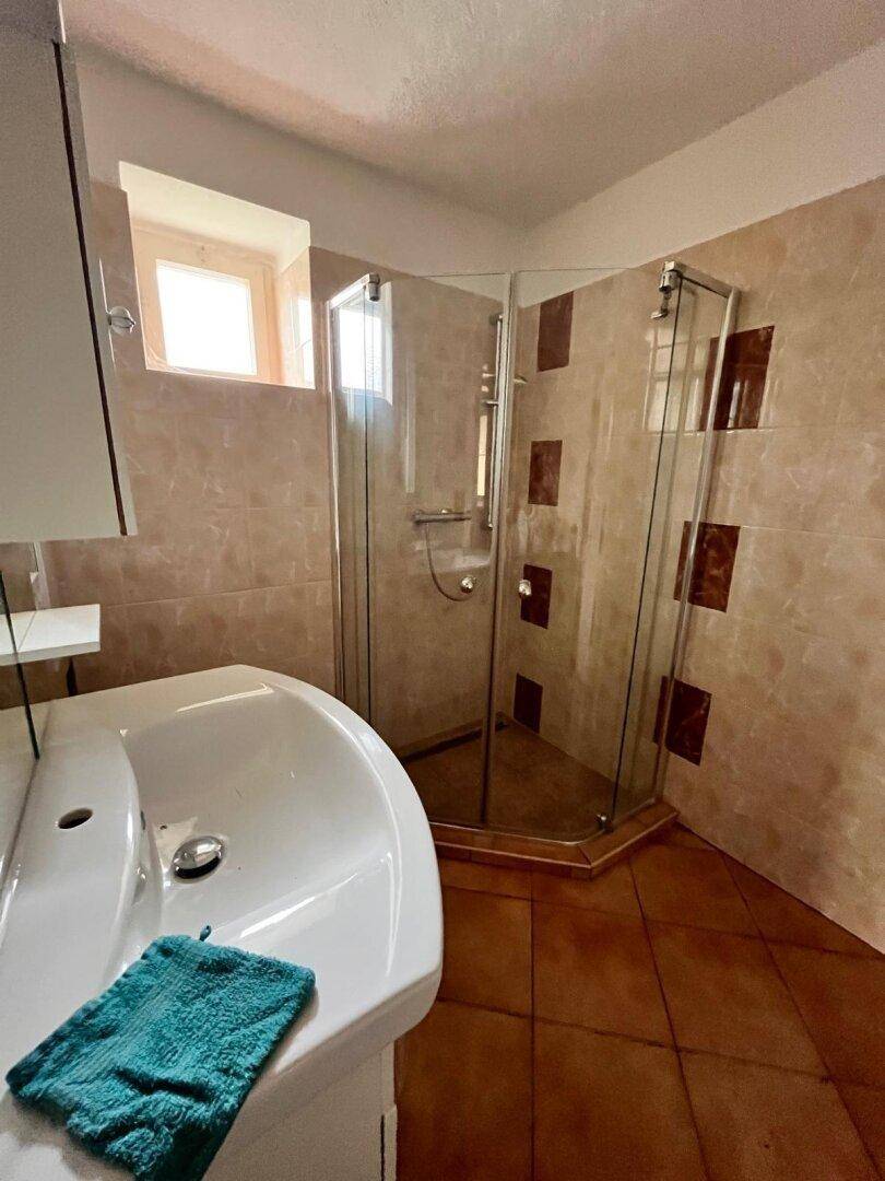 Badezimmer mit Duschkabine, Waschbecken und beigefarbenen Fliesen an Wänden und Boden.