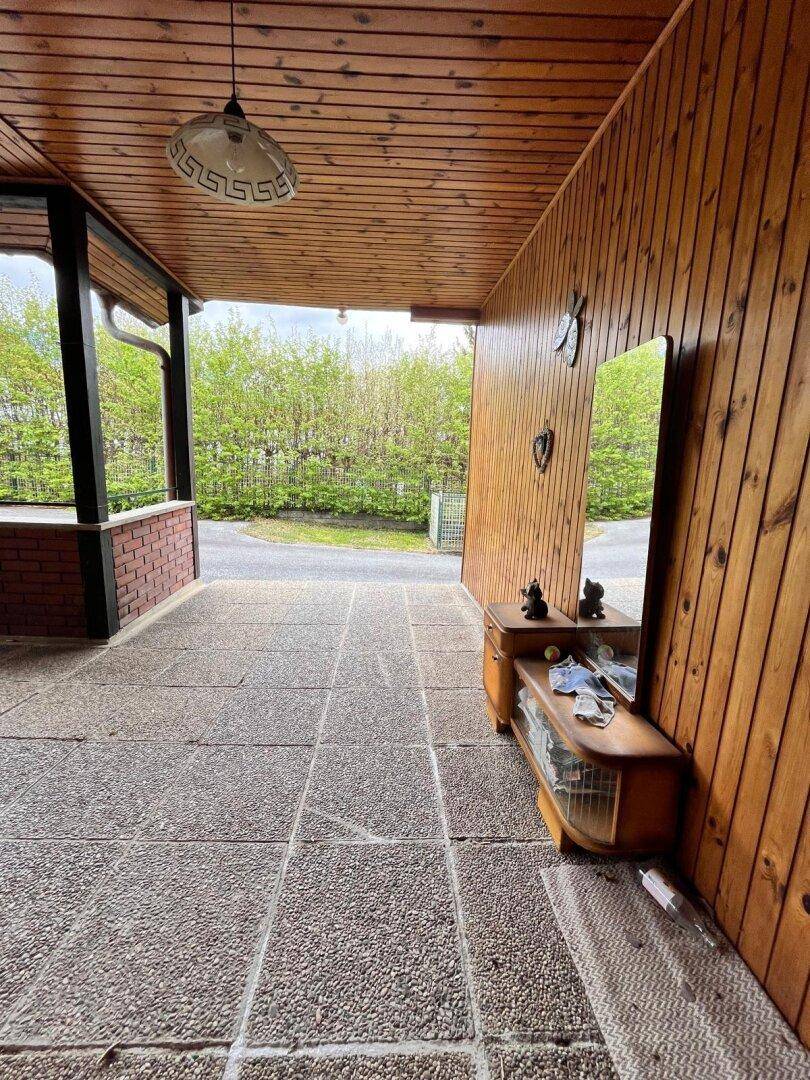 Überdachte Terrasse mit Holzdecke und -wänden, ausgestattet mit einem Spiegel und kleinem Schrank.