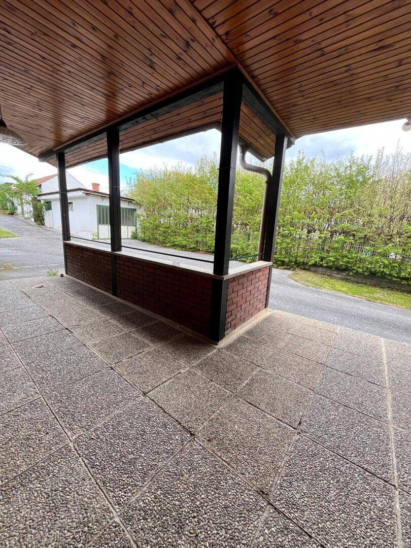 Überdachte Terrasse mit Betonplattenboden und Ziegelmauer, bietet einen Blick auf die Hecke.