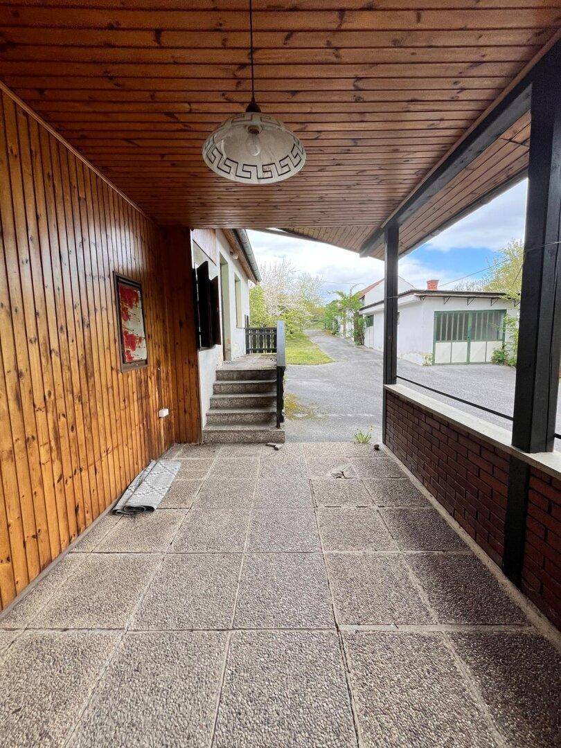 Überdachte Terrasse mit Betonplattenboden und Treppe zum Hauseingang, umgeben von Grün.