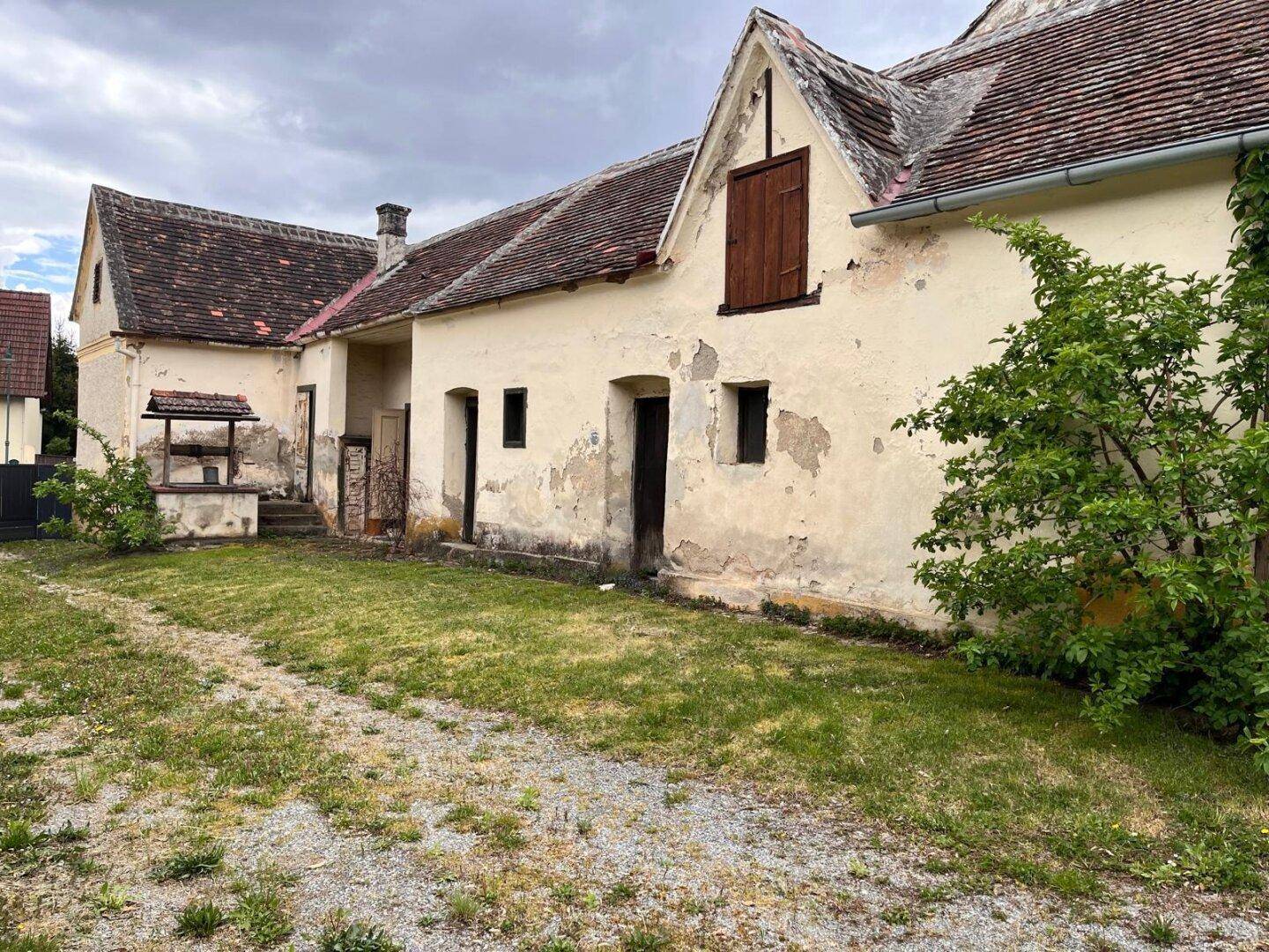 Altes Bauernhaus mit verputzter Fassade, Ziegeldach und einem traditionellen Brunnen im Hof.