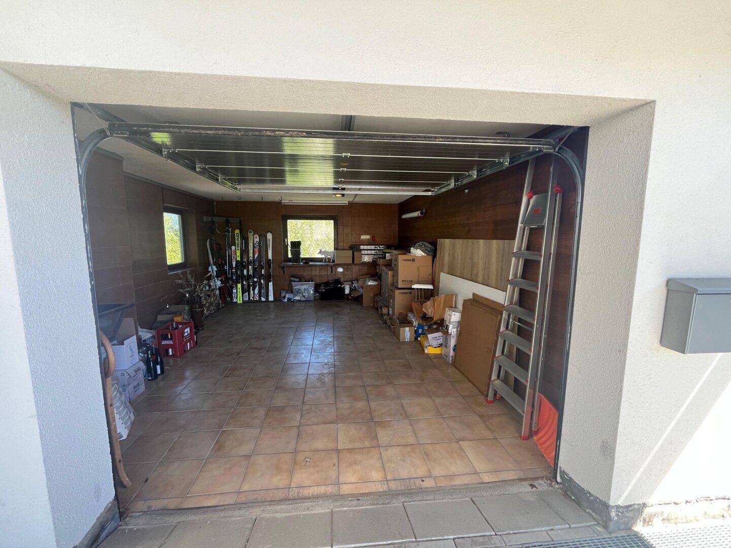 Geräumige Garage mit Fliesenboden, Stauraum und einem geöffneten Garagentor.