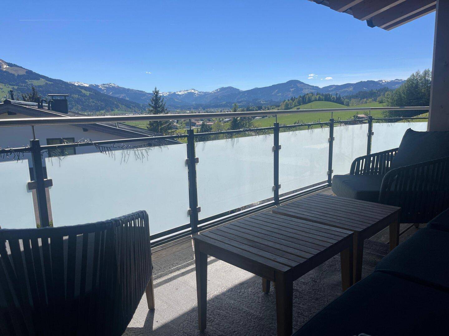 Sonniger Balkon mit Sitzgelegenheiten und weitem Blick auf die umliegende Berglandschaft.