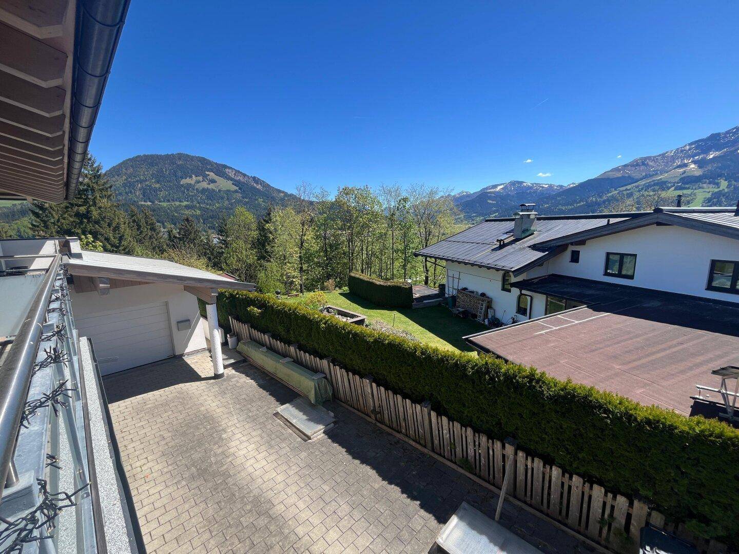 Panoramablick auf die umliegende Landschaft mit Häusern, Bäumen und Bergen im Hintergrund.