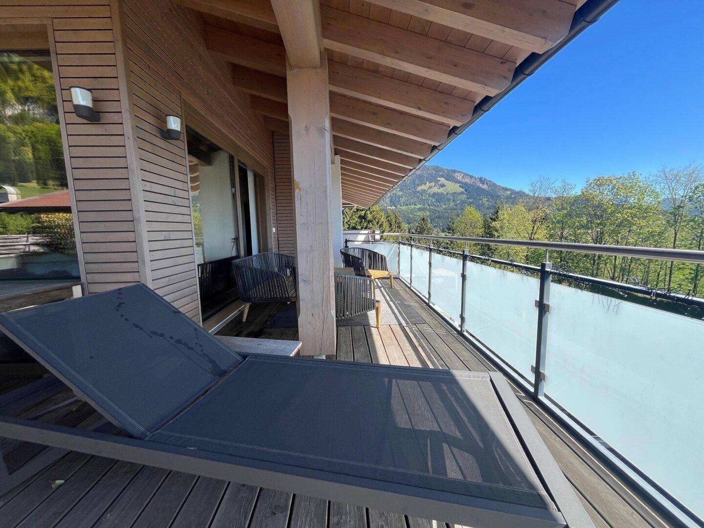 Langer Balkon mit Holzfußboden, Liege und Blick auf die grüne Berglandschaft.