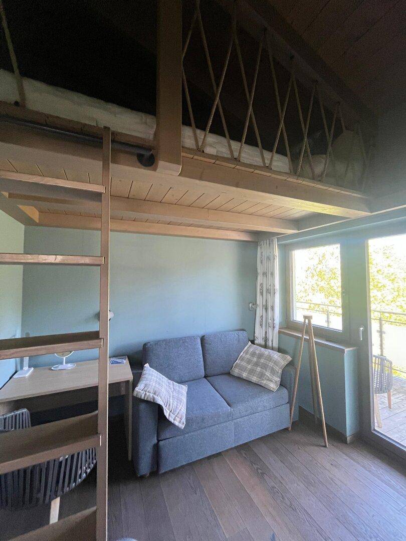 Gemütliches Schlafzimmer mit Schlafcouch, Schreibtisch und Hochbett in Holzkonstruktion.