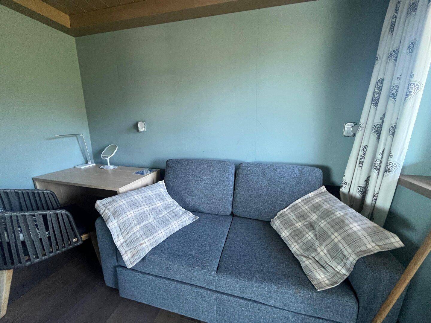 Helles Schlafzimmer mit Schlafcouch, Schreibtisch und Vorhängen in modernem Design.