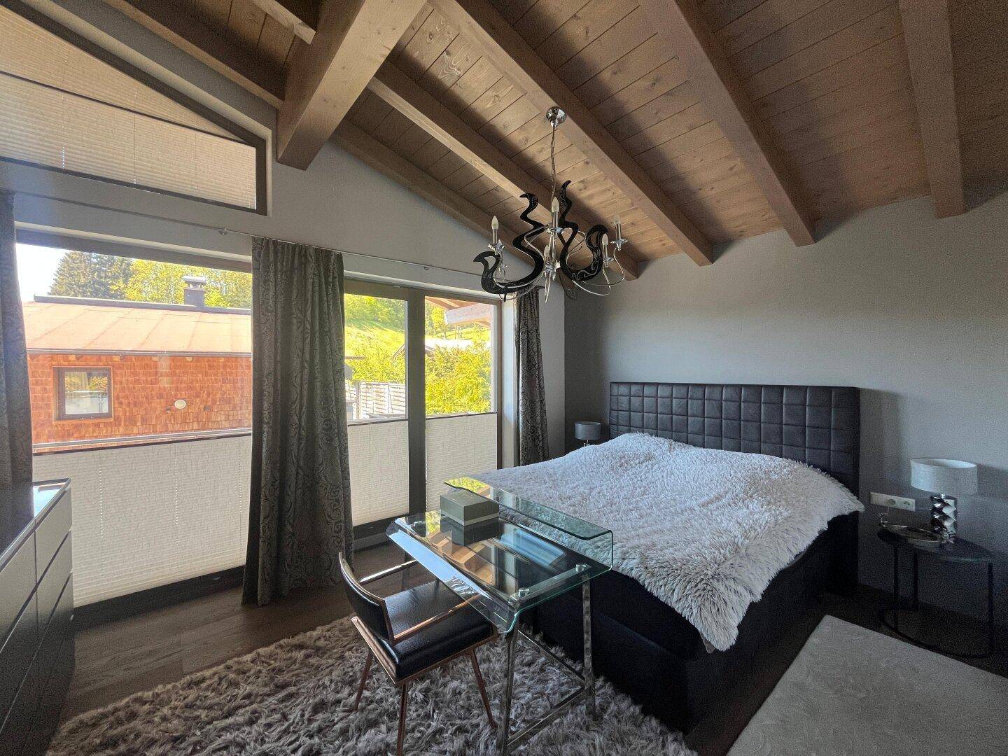 Geräumiges Schlafzimmer mit Doppelbett, Holzbalkendecke und großen Fenstern.