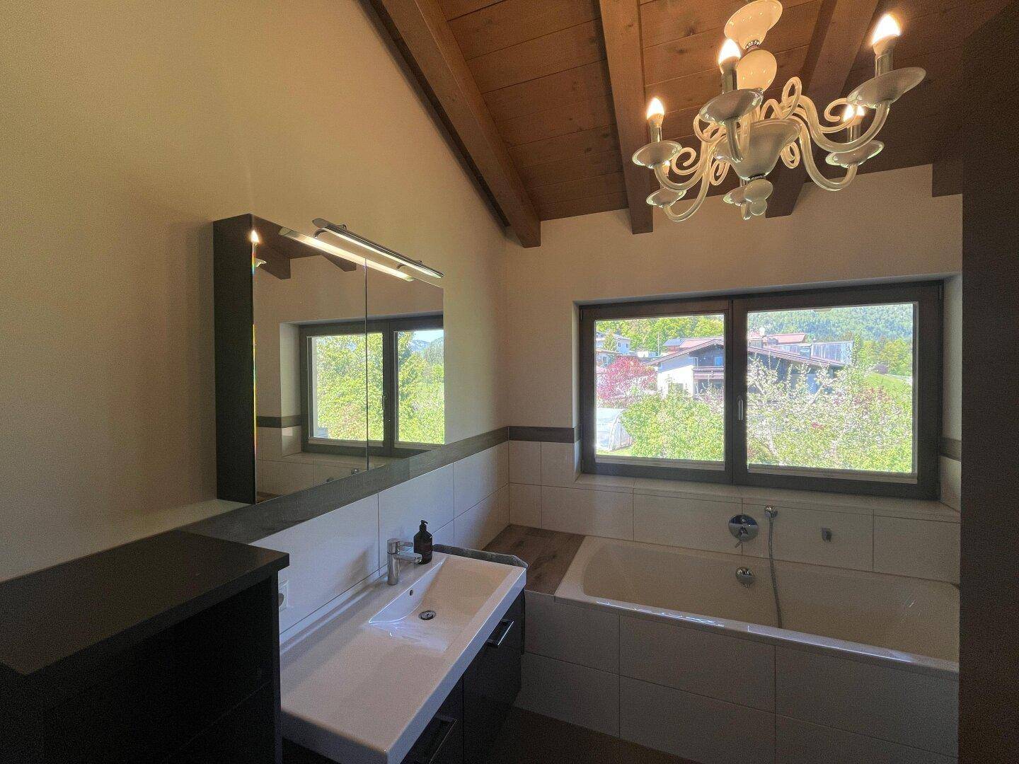 Helles Badezimmer mit Badewanne, Waschtisch und Dachschrägen, bietet einen schönen Ausblick ins Grüne.