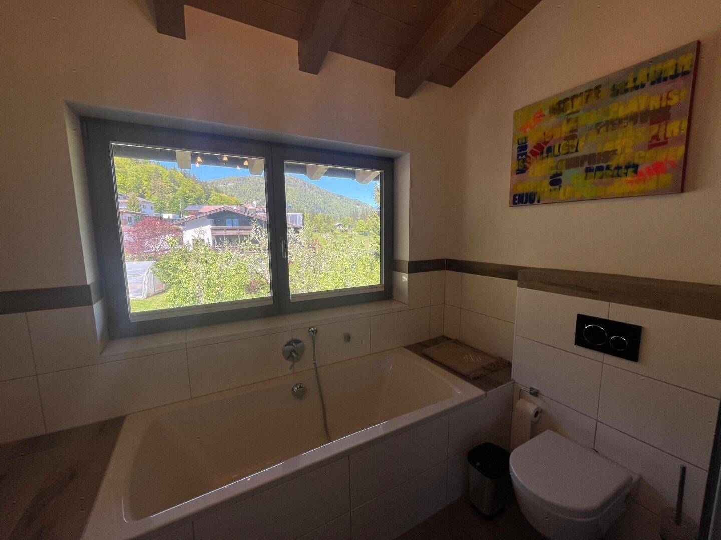 Badezimmer mit Badewanne, Toilette und Fenster, das einen weiten Blick auf die Berge und Landschaft bietet.
