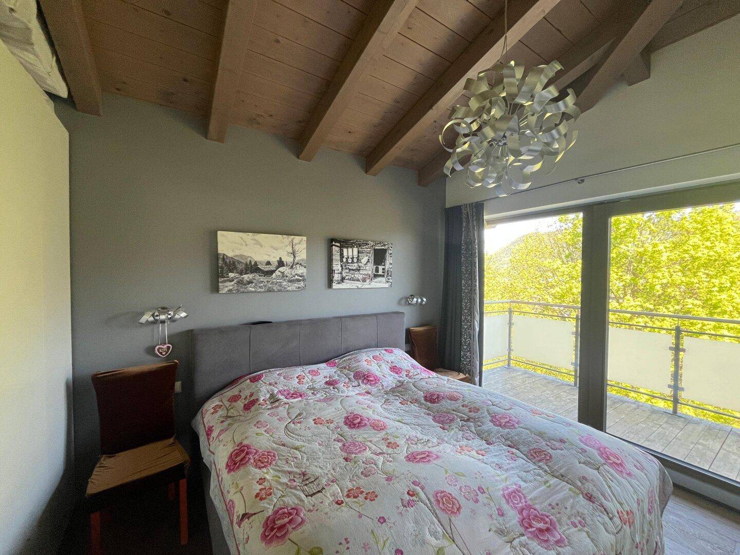Gemütliches Schlafzimmer mit Doppelbett, Holzbalkendecke und Zugang zu einem Balkon mit Bergblick.