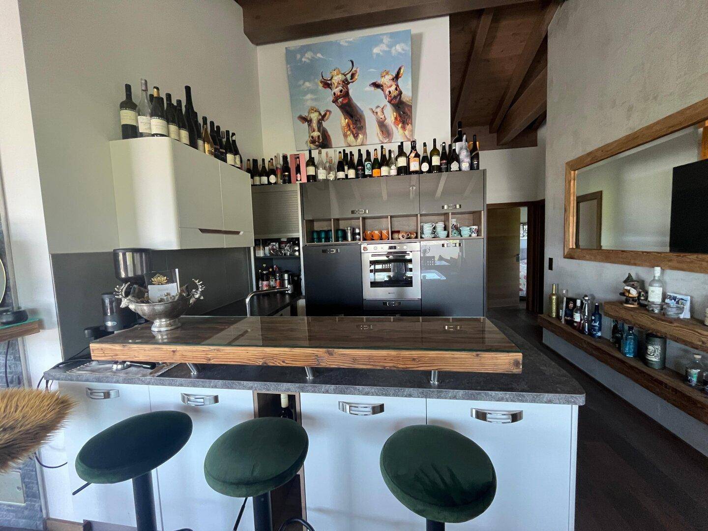 Offene Küche mit Bar und Hockern, integriert in einen Wohnbereich mit Holzbalkendecke.