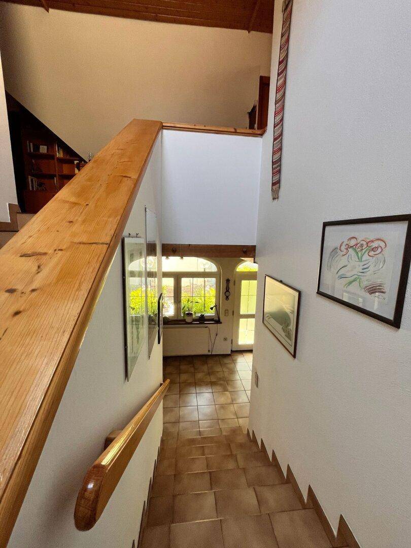 Holztreppe führt vom Obergeschoss in den hellen Eingangsbereich mit Fliesenboden.