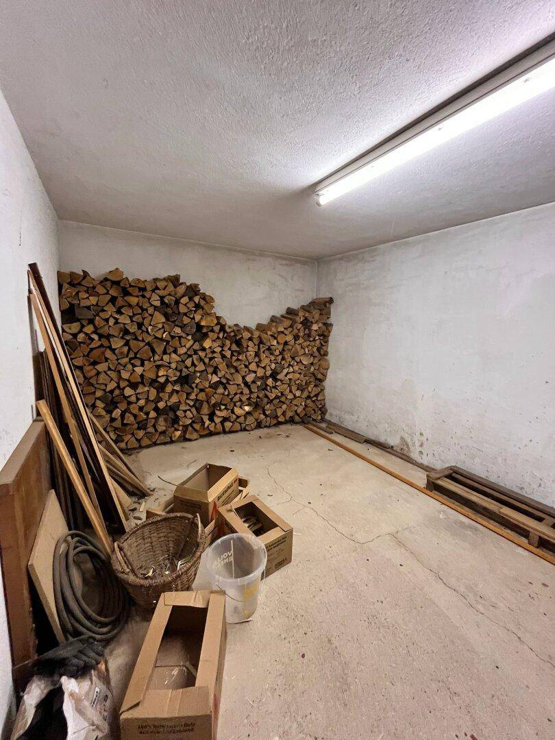 Lagerraum mit gestapeltem Brennholz und einfachem Betonboden.