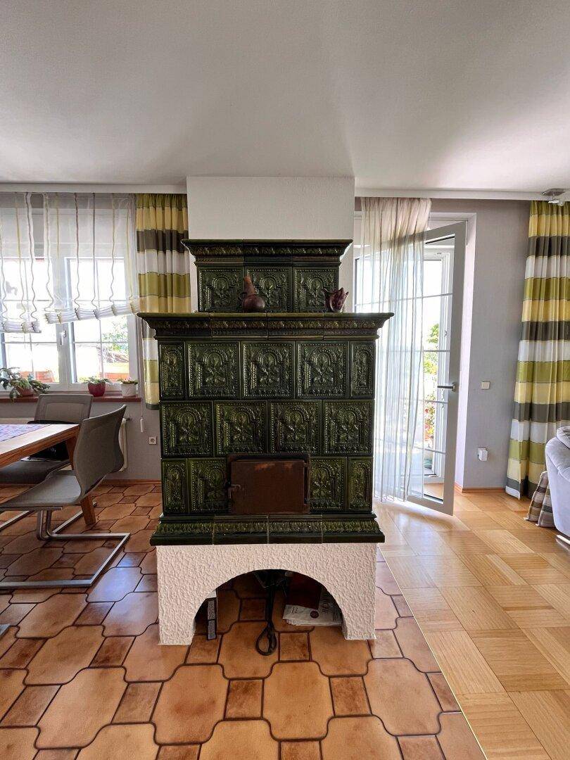 Detailansicht eines traditionellen grünen Kachelofens im Essbereich mit Terrakotta-Fliesenboden.