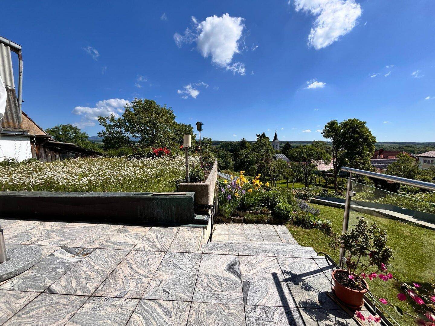 Geräumige Terrasse mit Steinplatten und weitem Blick über die Landschaft und ein Dorf.