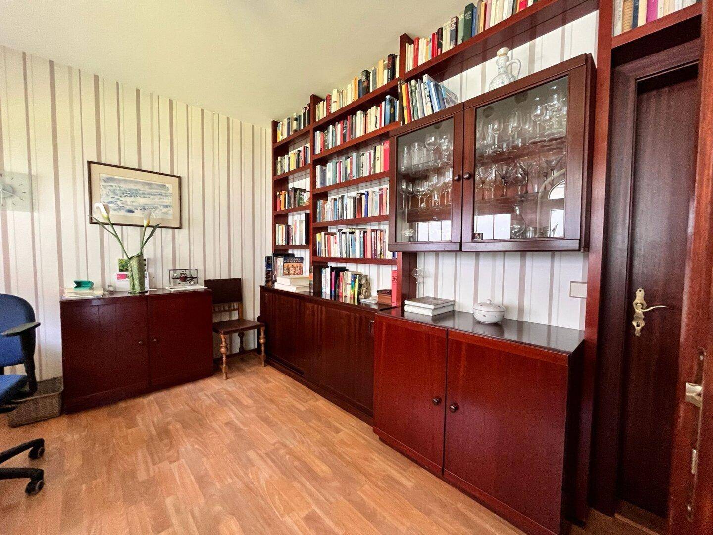 Arbeitszimmer mit umfangreichen Bücherregalen, dunklen Holzmöbeln und gestreifter Tapete.