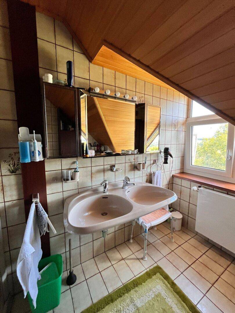 Badezimmer mit Doppelwaschbecken, Fliesenboden und Dachschräge, ausgestattet mit Spiegelschrank.