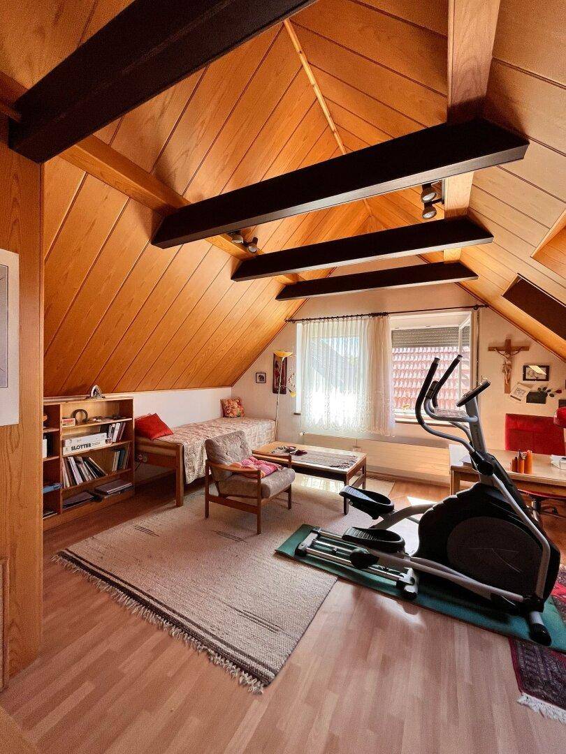 Schlafzimmer im Dachgeschoss mit Holztäfelung, Dachschrägen und einem Fitnessgerät.
