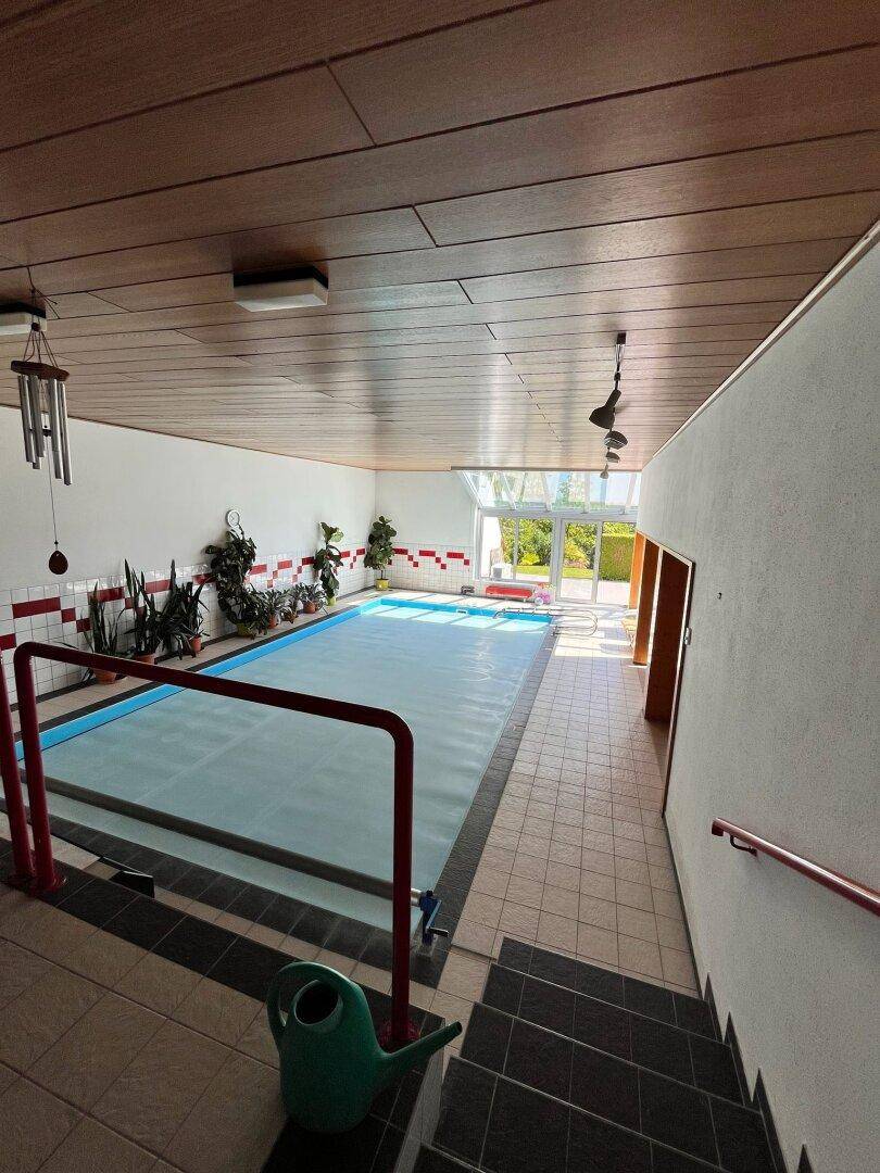 Geräumiges Hallenbad mit gefliestem Becken, Holzdecke und Treppenzugang.