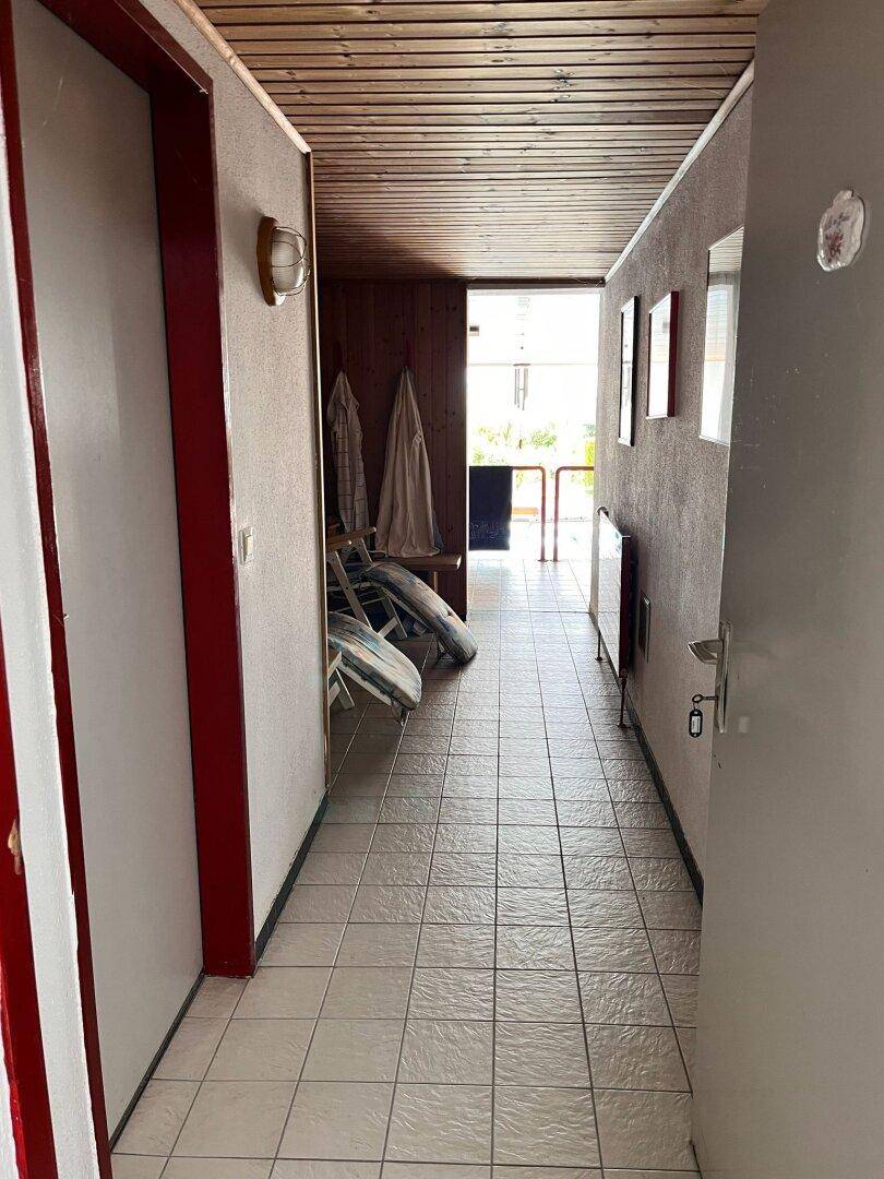 Langer Flur mit hellen Fliesen, Holzdeckenverkleidung und Zugang zu weiteren Räumen.