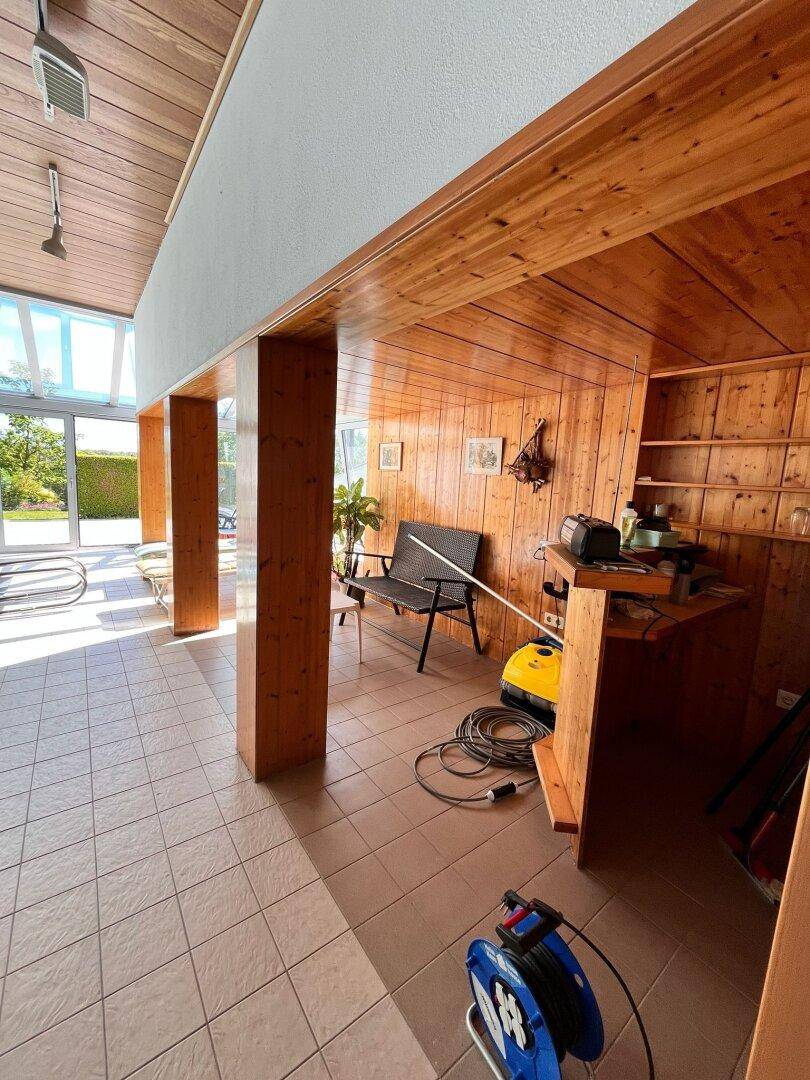 Entspannungsbereich neben dem Pool mit Holzverkleidung, Fliesenboden und viel Tageslicht.