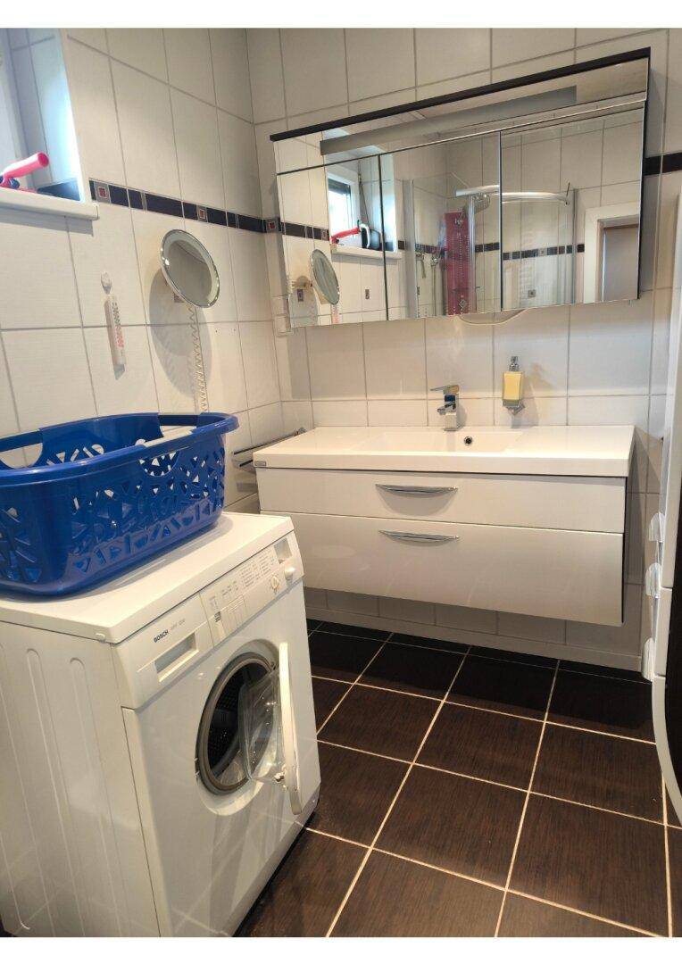 Modernes Badezimmer mit dunklen Fliesen, Doppelwaschbecken und einer Waschmaschine.