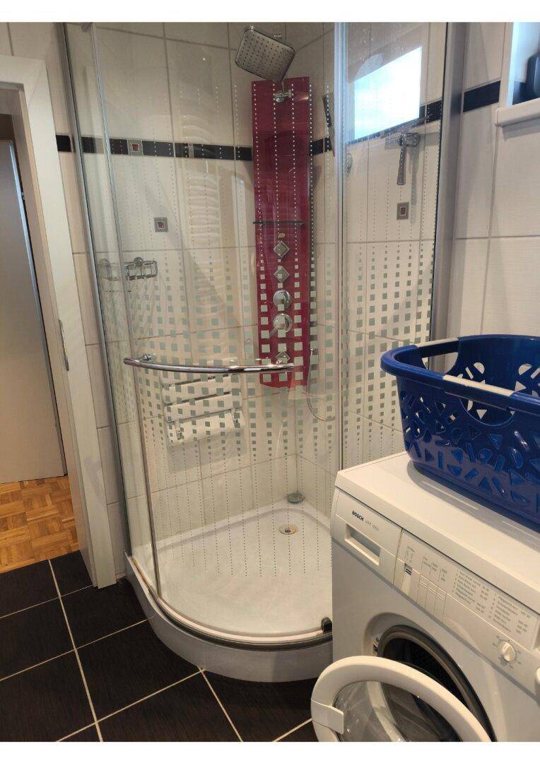 Badezimmer mit Eckduschkabine, dunklem Fliesenboden und einer praktischen Waschmaschine.