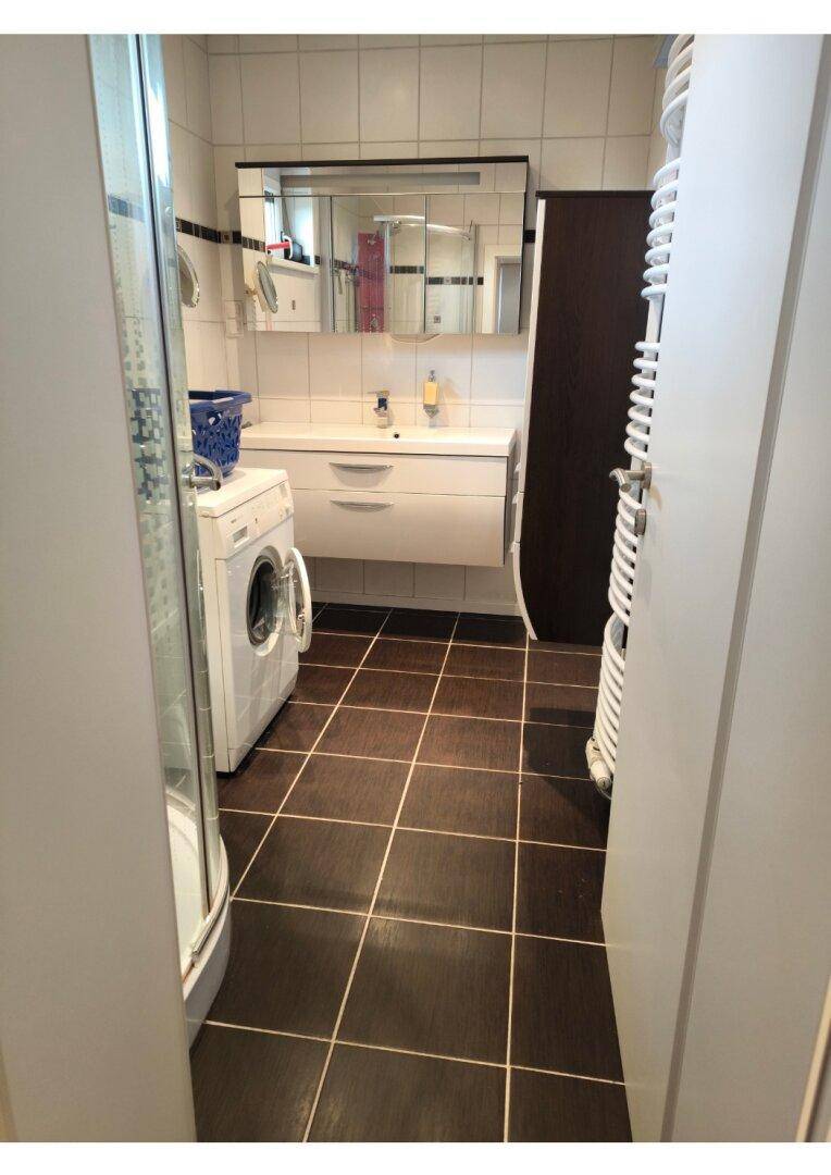 Badezimmer mit dunklem Fliesenboden, weißem Waschtisch, Spiegelschrank und beheiztem Handtuchhalter.