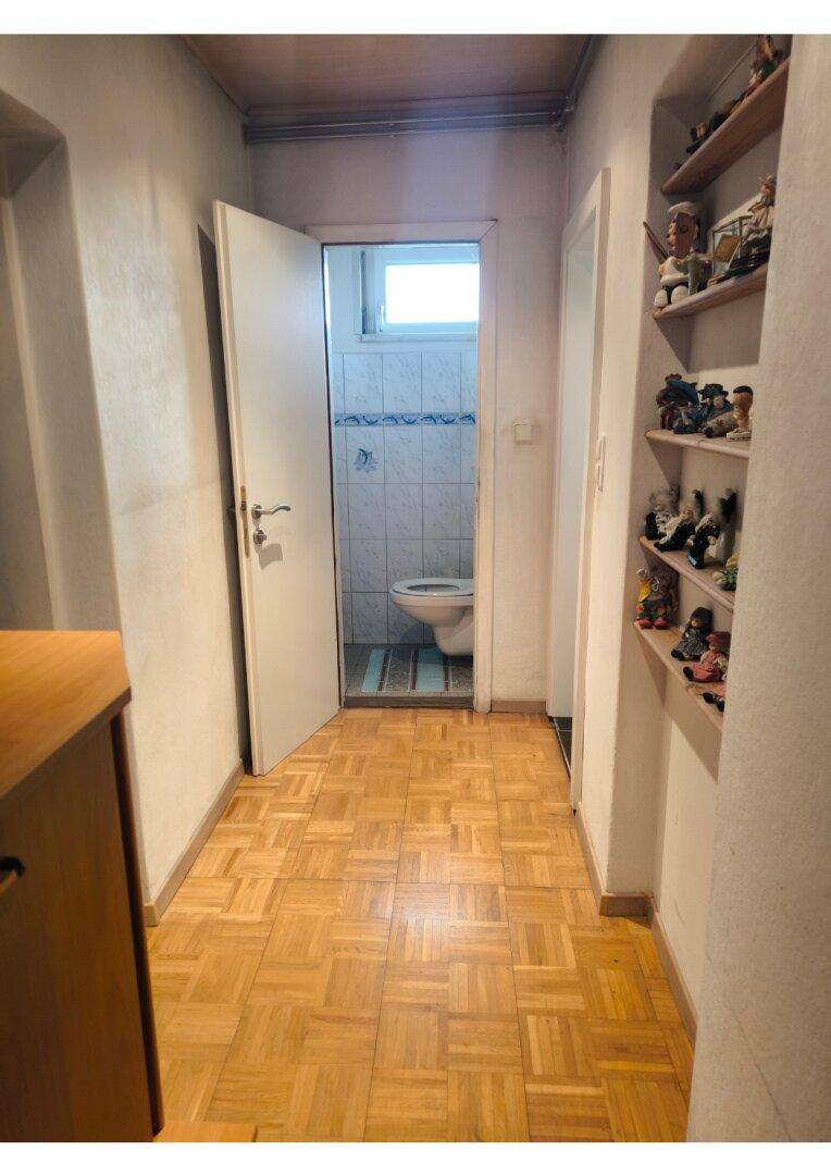 Flur mit Parkettboden, der zu einem separaten WC mit Fenster führt.