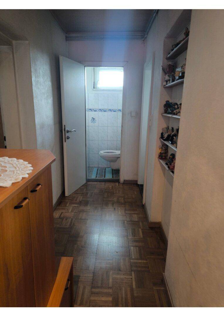 Flur mit Parkettboden, der zu einem separaten WC mit Fenster führt.