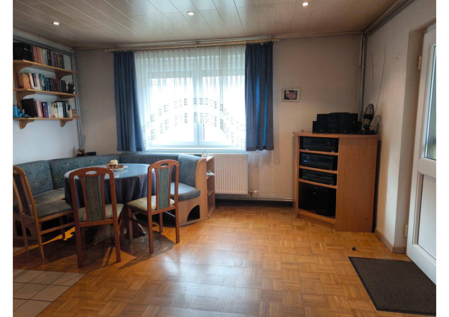 Gemütlicher Wohn-Essbereich mit Eckbank, Parkettboden und einem großen Fenster.