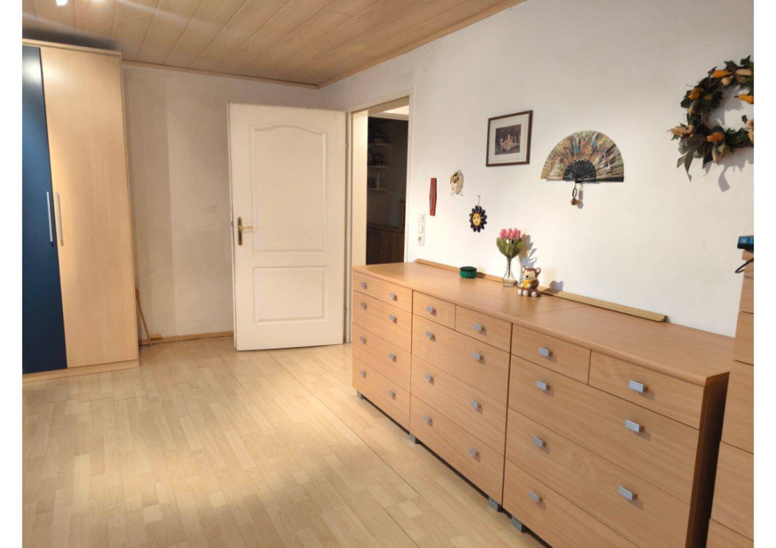 Schlafzimmer mit hellem Holzfußboden, einer langen Kommode und einem Kleiderschrank.